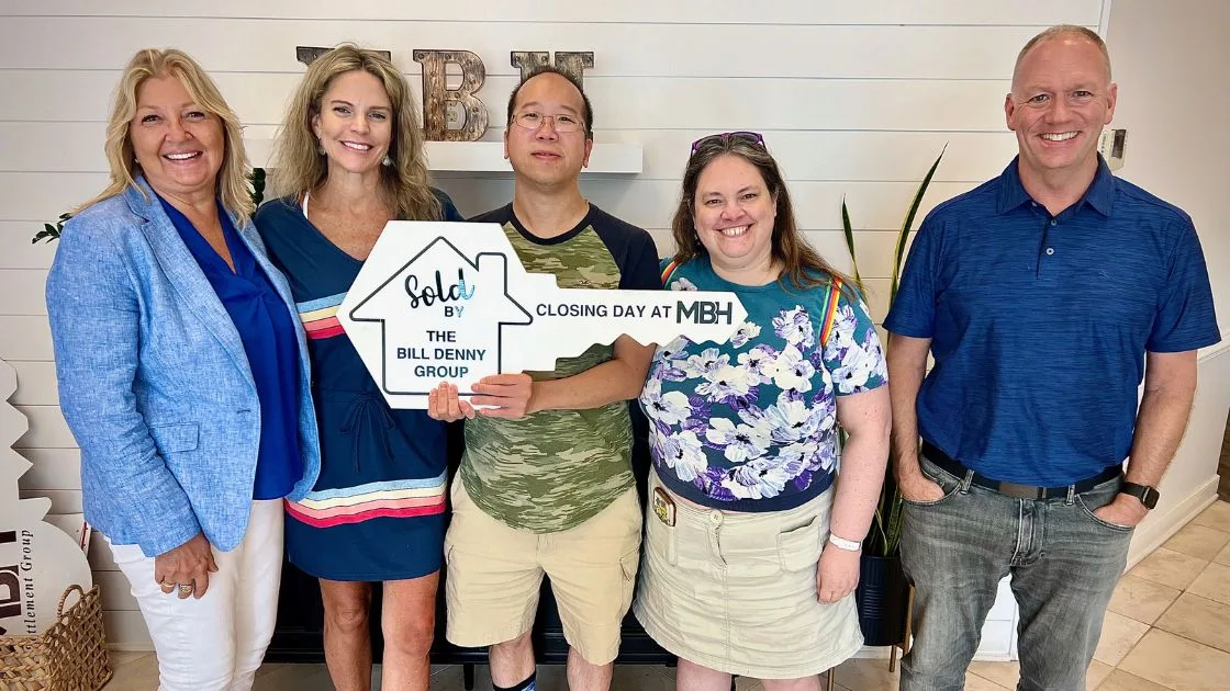 The Bill Denny Real Estate Group with buyers holding a Sold by The Bill Denny Group key sign on closing day at MBH Settlement Group