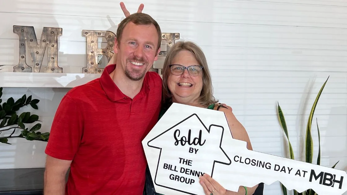 Happy clients holding a Sold by The Bill Denny Group key sign on closing day at the MBH Settlement Group office
