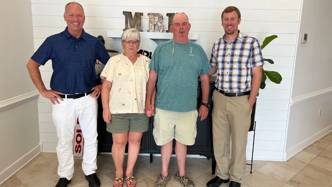 The Bill Denny Real Estate Group with buyers holding a SOLD sign at the MBH Settlement Group office after closing