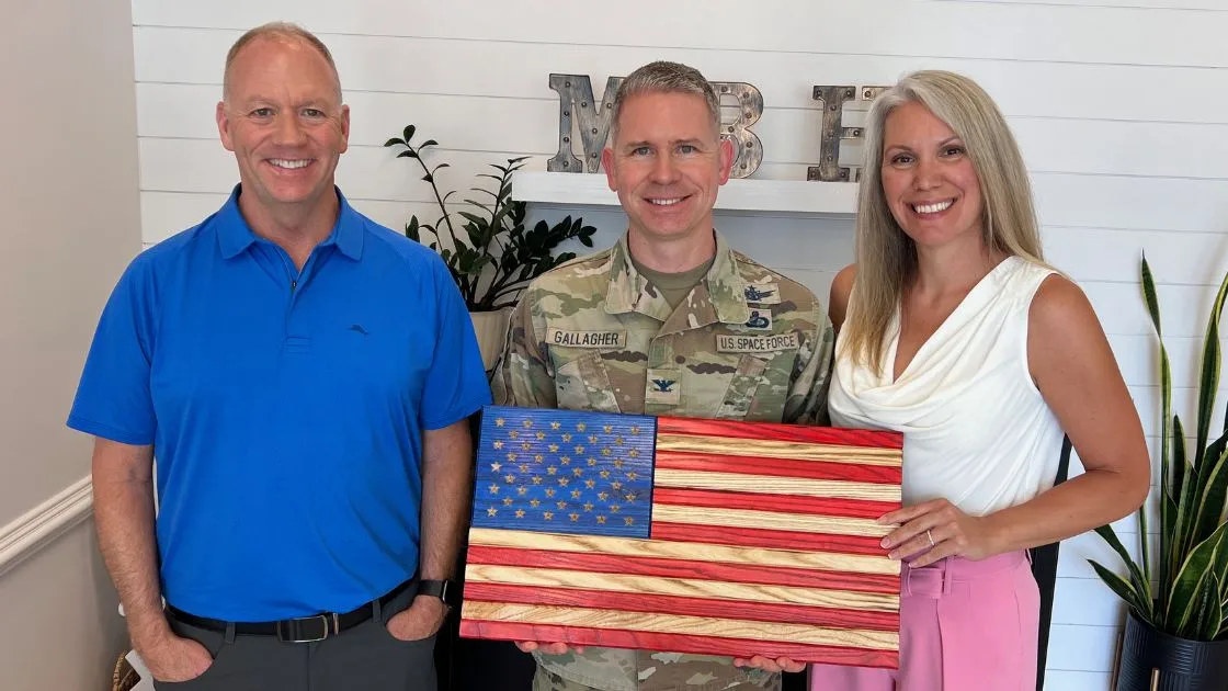 The Bill Denny Real Estate Group with a U.S. Space Force service member holding a handcrafted wooden American flag